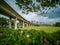 Train bridge in Jurong, Singapore, with green vegetation in front and blue cloudy sky in background