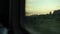 A train goes in the countryside. View from the window. Travelling by train at sunset. View of green grass and trees from