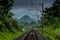 Train lines with green landscape view, forested mountains and cloudy sky background