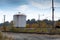 Train tracks alongside gravel access road and industrial tank, power lines, fall season