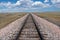 Train Tracks on an Open Plain Stretching Out to a Blue Sky and Clouds on the Horizon