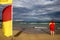 Trained competent female lifeguard beach patrol wearing red yellow shirt standing on the beach watching ensuring tourists swimming