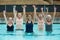 Trainer and senior swimmers lifting dumbbells in swimming pool