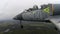 A training gray blue fighter plane fly high above the forest against a dark overcast cloudy sky. The chassis open and lowers.