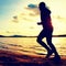 Training at sunset.Running tall man. A silhouette of jogger at path along lake coastline.