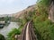 Trains-eye view of railroad tracks going through a rocky pass mountain near river.