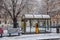 Tram bus stop under the snow in winter day, yellow ticket machine, christmas atmosphere, trees and blue wooden benches at Kinsky