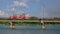 Tram moves along the bridge over the river on background of blue cloudy sky.