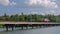 Tram moves along the bridge over the river in a city on a background of green trees.