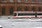 Tram rides along brick building, snowing