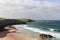 The tranquil beauty of Durness Beach with pristine sands meeting crystal-clear waves, edged by cliffs and lush greenery