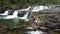 Tranquil creek cascading down a jagged landscape of moss-covered rocks and lush foliage