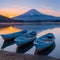 Tranquil lake scene at sunset with rowboats moored along shore with majestic silhouette snowy volcano in background. serene