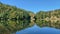 Tranquil landscape of a river, with the reflection of a lush forested shoreline, and tall trees