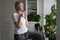 Tranquil middle-aged lady drinks hot drink from mug at windowsill looking out of window