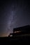 Tranquil night sky illuminated by a bright, milky way backdrop, with a cozy house