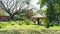 Tranquil park scene with a thatched gazebo surrounded by lush greenery and in the foreground