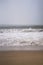 Tranquil sandy beach on a sunny day, with rolling white-crested waves coming in towards the shore