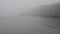 Tranquil sea on foggy day with cliffs in background.