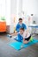 Tranquil short-haired patient holding blue dumbbell while sitting on the mat