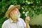 Tranquility and serenity. Harmony of soul. Elderly man in straw summer hat. Lonely grandpa blowing dandelion seeds in