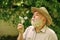 Tranquility and serenity. Harmony of soul. Elderly man in straw summer hat. Lonely grandpa blowing dandelion seeds in