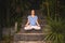 Tranquility woman sitting on stone stairs in lotus position practicing yoga mudra at tropical garden