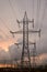 Transmission tower silhouette and high voltage overhead transmission lines, at sunset, with fiery orange skies and stormy clouds