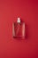 Transparent bottle of perfume with spray on red surface.