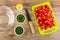 Transparent bowl, salt, bowls with chopped scallion and dill, knife, pieces of tomatoes on cutting board on table. Top view