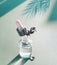 Transparent cosmetic bottle with pipette standing on blue background with palm leaves shadow. Facial skin care concept. Natural