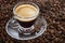 A transparent cup with aromatic frothy coffee stands on the beans. Close-up