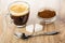 Transparent cup with coffee espresso, bowl with ground coffee, sugar, spoon on wooden table