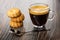 Transparent cup with coffee espresso, stack of shortbread cookies, spoon on wooden table