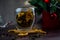 A transparent cup of tea stands on a dark table, on a wooden stand, dried orange slices float in the cup, citrus slices