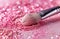 a transparent eyeshadow brush against pink paper with glitter splatter