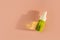 Transparent glass dropper bottle with green liquid inside on beige pink background in the sunlight