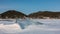 Transparent glittering ice floe in the middle of a frozen and snow-covered lake.