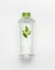 Transparent liquid bottle with green lid. Clean nature water with green leaves and branding mock up on white desk