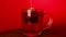 Transparent mug of black tea on red background. Unrecognizable person dipping tea bag in mug. Concept of fast brewing