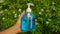 A transparent plastic bottle of blue alcohol gel for anti bacteria, germ and virus in a woman person hand, green leaves of