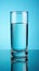 Transparent tall glass with water standing on table with blue background