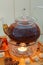Transparent teapot kettle with tasty black tea on stand with candles. On tray cinnamon, sugar, anise and orange. On wooden backgro