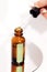 Transperent drop of essence, oil or gel drips from the pipette. Blurred brown glass serum bottle on the background