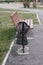 The trash can is damaged, broken in the Park near the bench. Vandalism