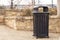 Trash can in park alongside stone brick wall on gravel walkway