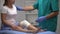 Traumatologist checking female knee in elastic wrap during examination, trauma