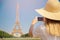 Travel blogger young woman in hat takes photograph of Eiffel Tower on telephone in Paris, France