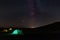 Travel and camping concept - three glowing camping tents at night under a starry sky with milky way and setting sun.