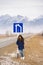 Travel destination. Girl leans on road sign on mountains background